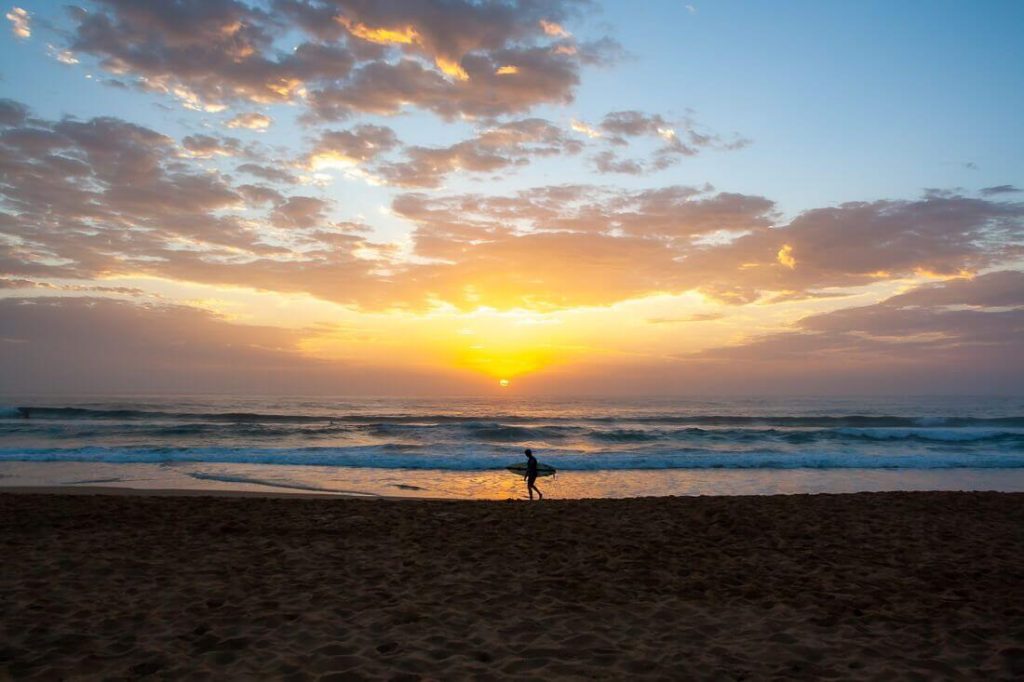 Surfer walking along Avoca Beach at sunrise on the Central Coast