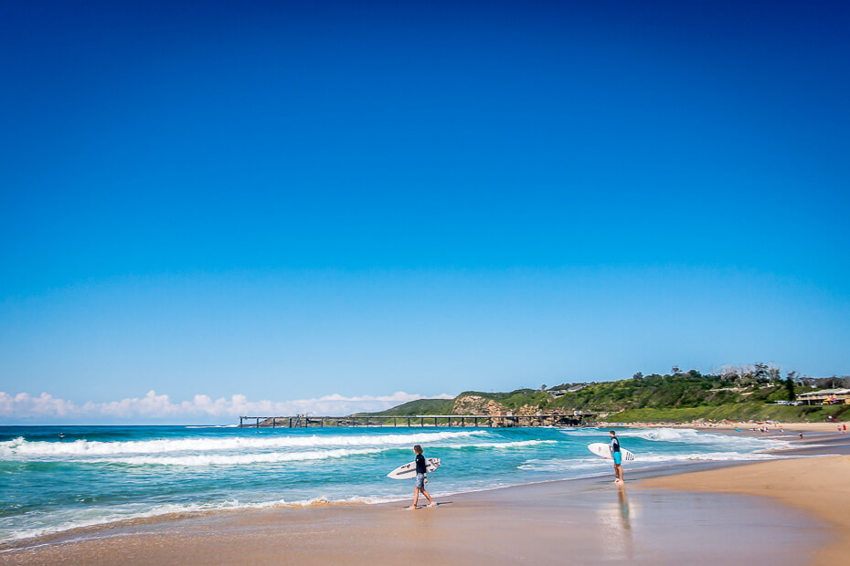 Surfers walking along Catherine Hill Bay beach in Lake Macquarie