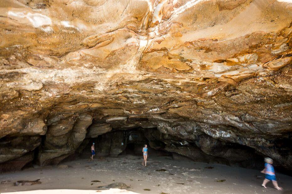 Visitors walking inside a large sea cave at Caves Beach during low tide
