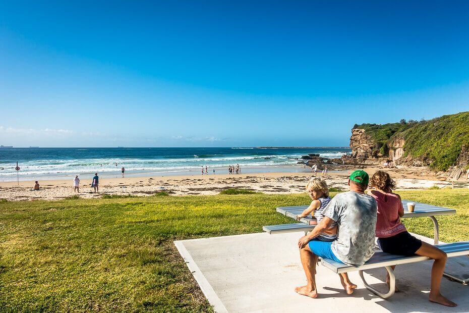 Family enjoying a picnic at Caves Beach with ocean and cliff views in the background