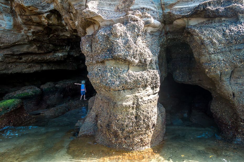 Rock pillars and cave openings at Caves Beach with a person standing inside at low tide