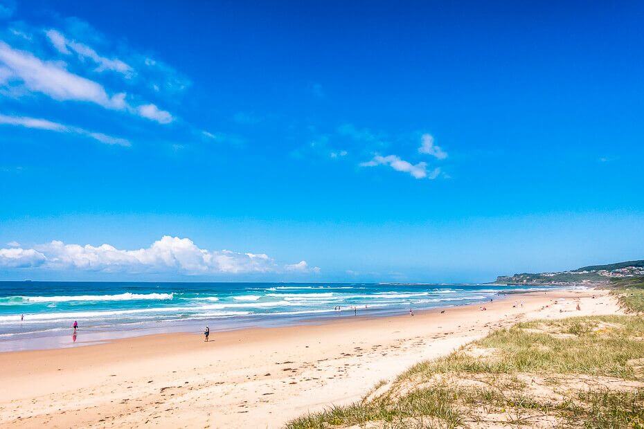 Wide sandy beach at Caves Beach with people swimming and surfing in the ocean