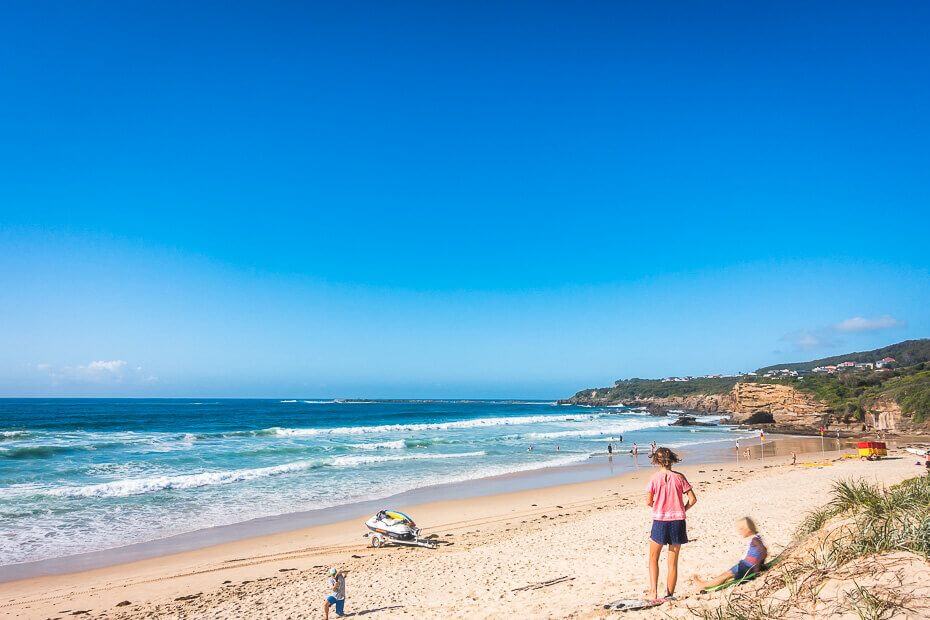 People swimming and enjoying the waves at Caves Beach on a clear sunny day