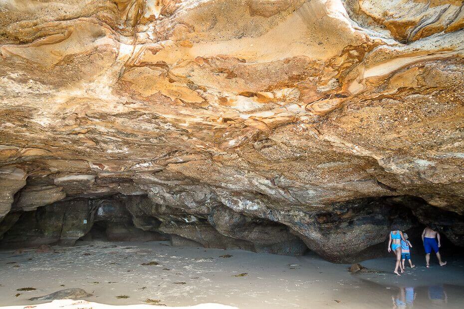 Visitors walking through the sea caves at Caves Beach at low tide