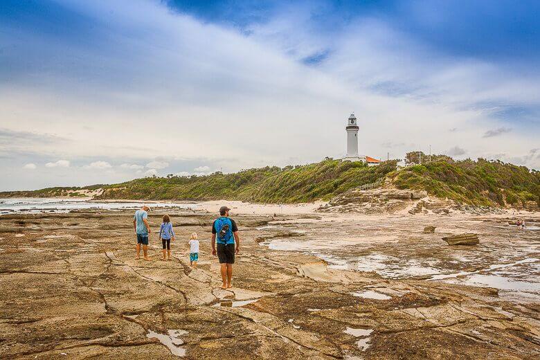 Family walking across the rock platform toward Norah Head Lighthouse on the Central Coast NSW