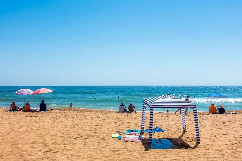 Striped beach tent providing shade on a sunny Australian beach.