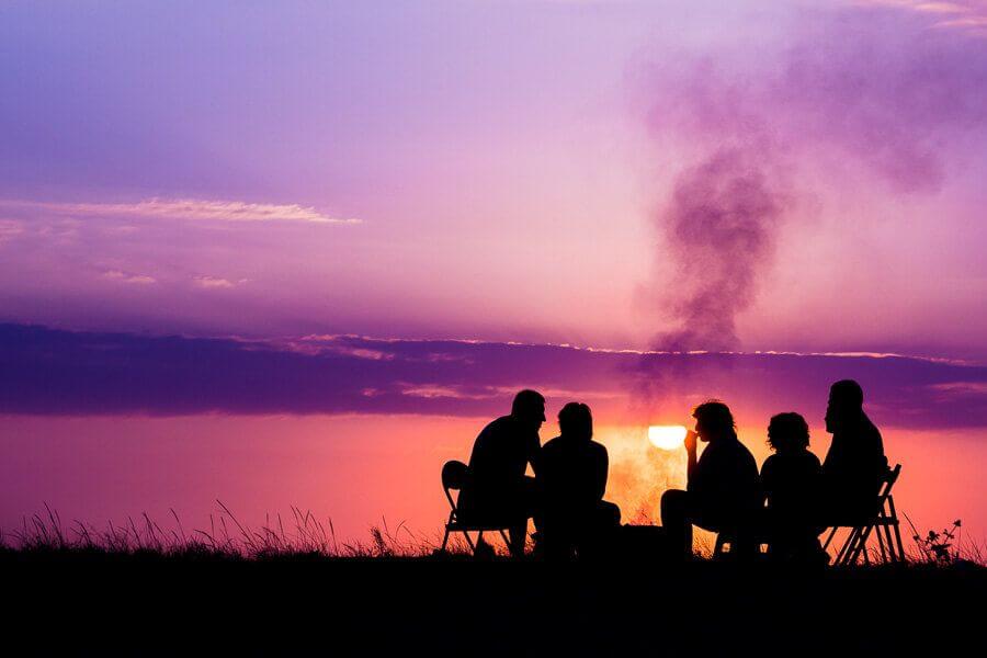 People sitting on camping chairs around a campfire at sunset