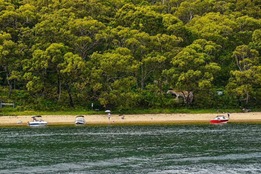 Small boats moored off the sandy shore of Lobster Beach in Bouddi National Park.
