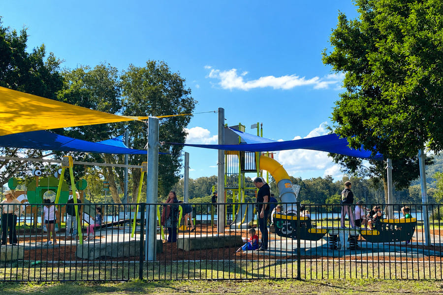 Fenced playground with slides, swings and shade sails at Lions Park in Woy Woy