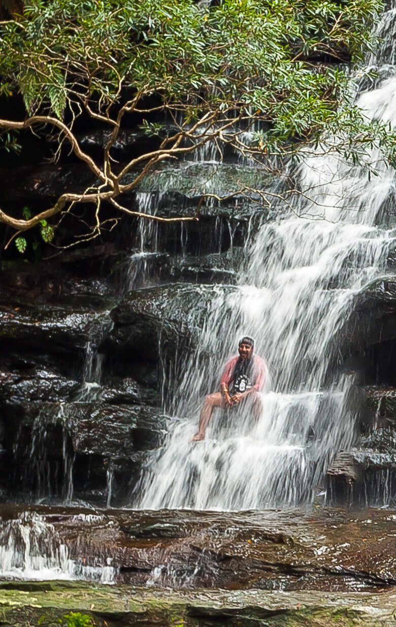 Visitor sitting beneath the cascading waterfall at Somersby Falls