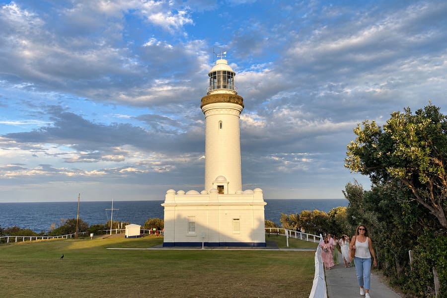 Norah Head Lighthouse viewed from the front lawn with ocean behind and visitors walking along the path