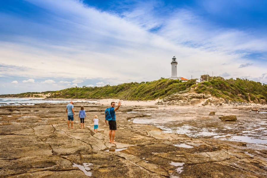 Family walking across the rock platform below Norah Head Lighthouse at low tide