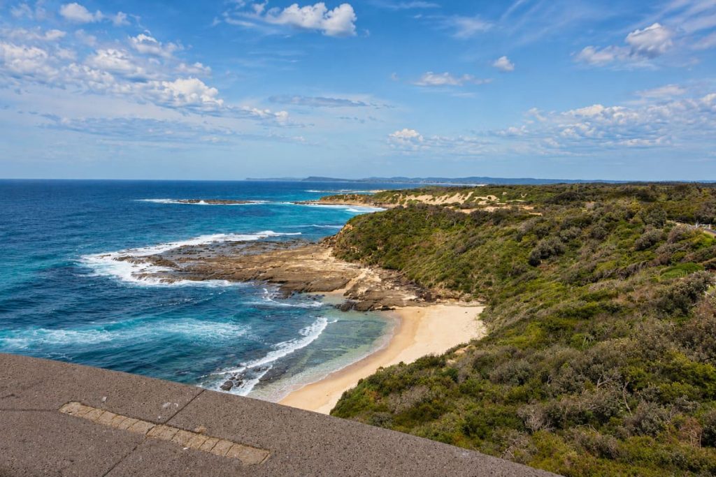 Coastal view from the top of Norah Head Lighthouse showing rocky shoreline, beach, ocean and surrounding bushland