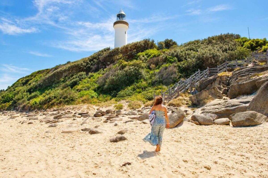 Woman walking along the beach below Norah Head Lighthouse near the stairs and rocky shoreline