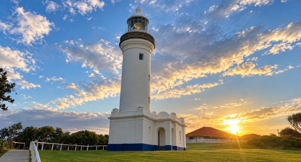 Norah Head Lighthouse at sunset with golden light across the lawn and clouds