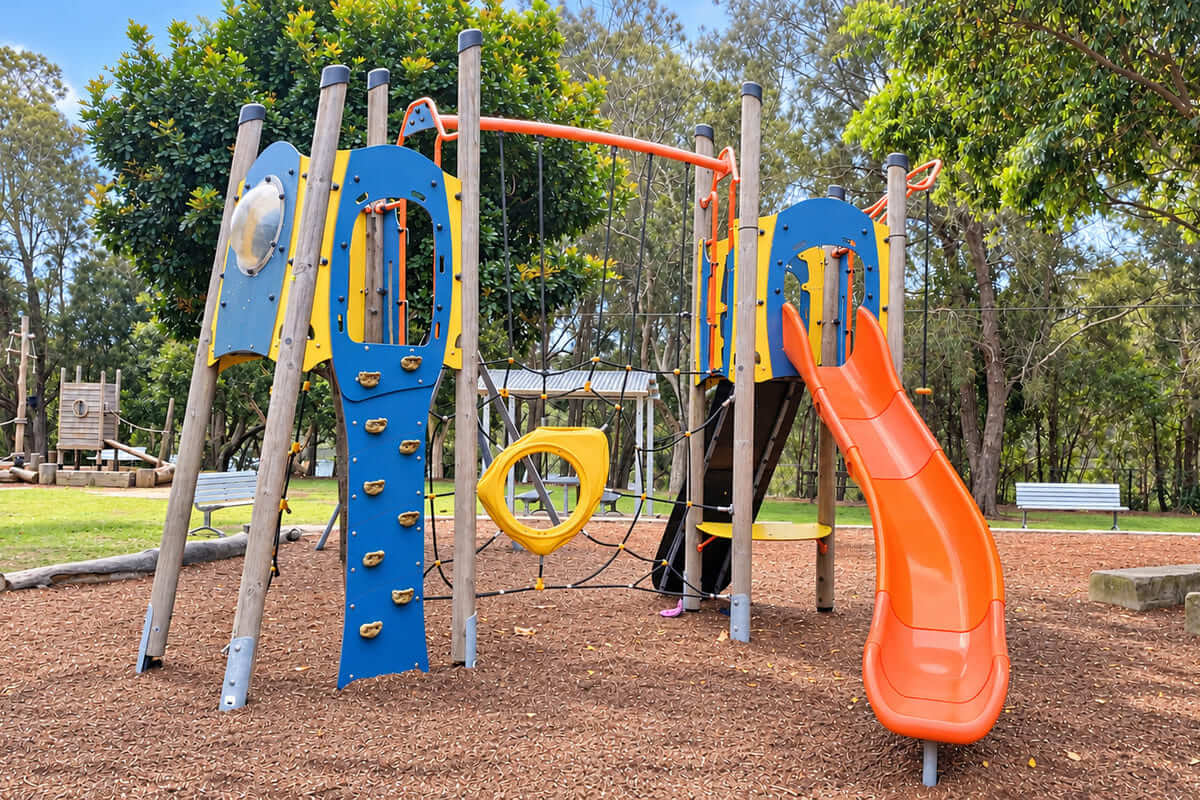 Terrigal Rotary Park playground with an orange slide, blue climbing wall, rope net and timber play structures